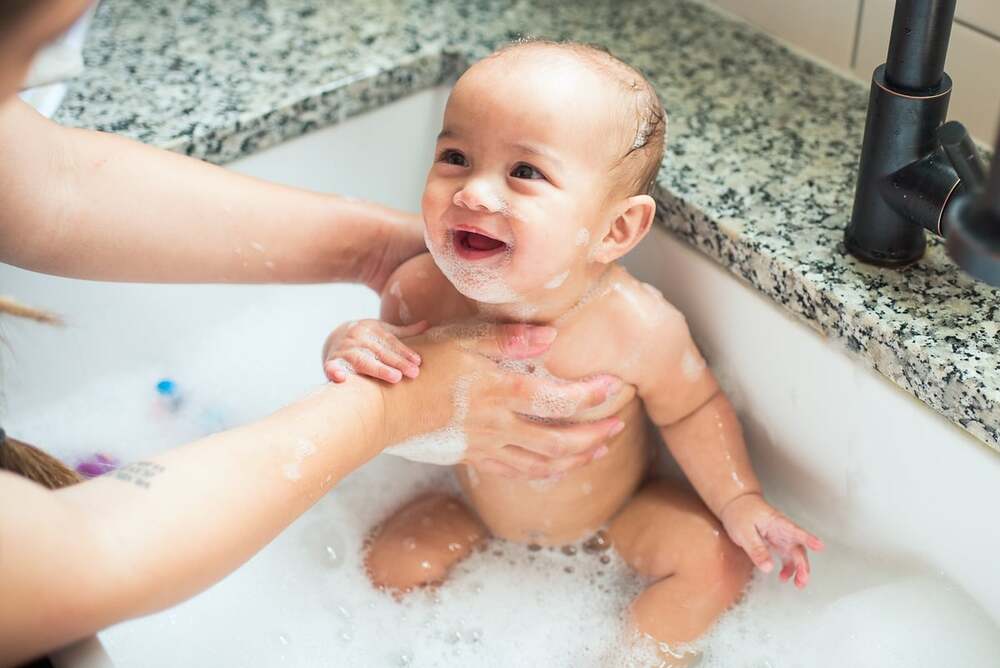 Mother giving her baby a bubble bath while the baby is smiling.