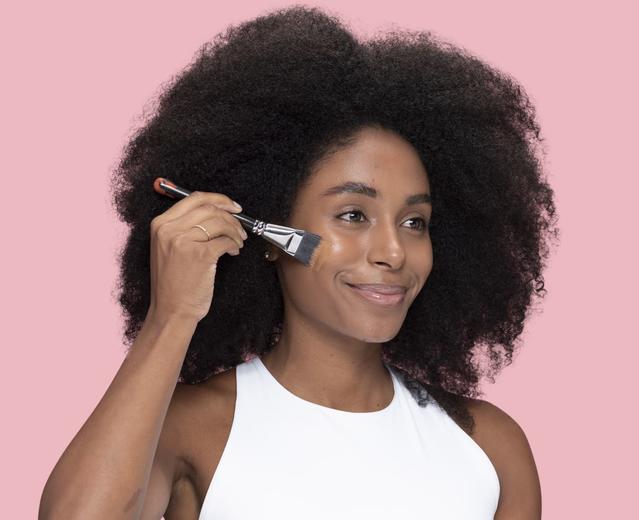 Woman looking at the mirror smiling and applying a skincare product with a brush